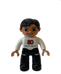 Duplo Figure Lego Ville, maschio, gambe nere, top bianco, capelli neri, '80 evesek vagyunk 'sul davanti, logo LEGO sul retro